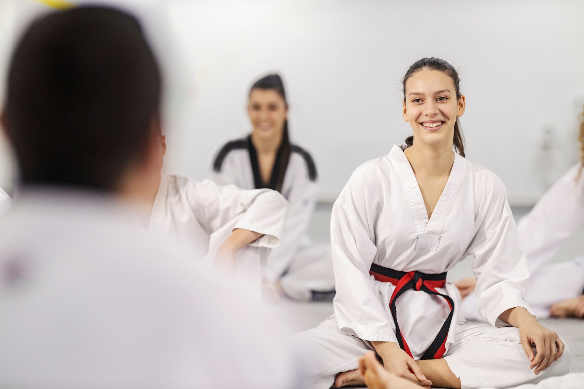 Portrait of a happy taekwondo athlete sitting at martial school class and smiling at the trainer.